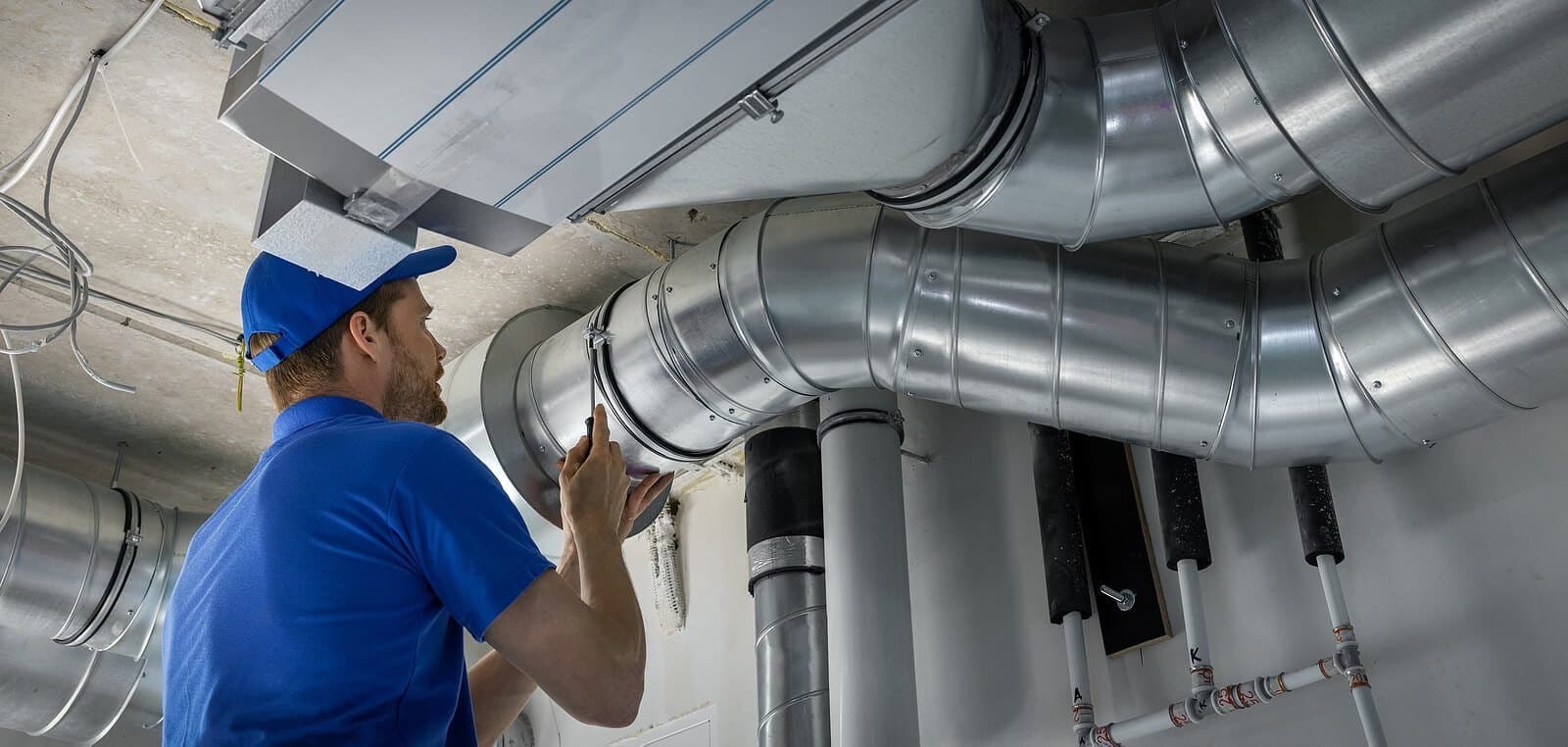 Technician installing HVAC ductwork in industrial setting.
